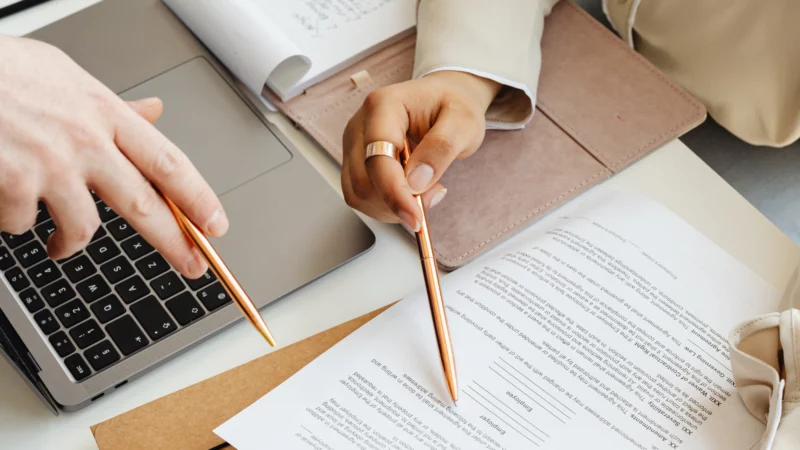 Personnes en train d’examiner des documents et un contrat sur ordinateur dans le cadre d’une acquisition d’entreprise.